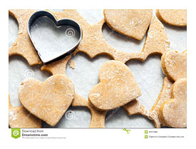 Heart Shaped Cookie Cutter On Raw Cookie Dough With A Few Cookies