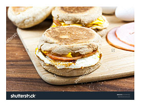 English Muffin, Egg, Ham, And Cheese Breakfast Sandwich On A Cutting